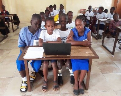 three children in Africa look at a laptop computer in a classroom