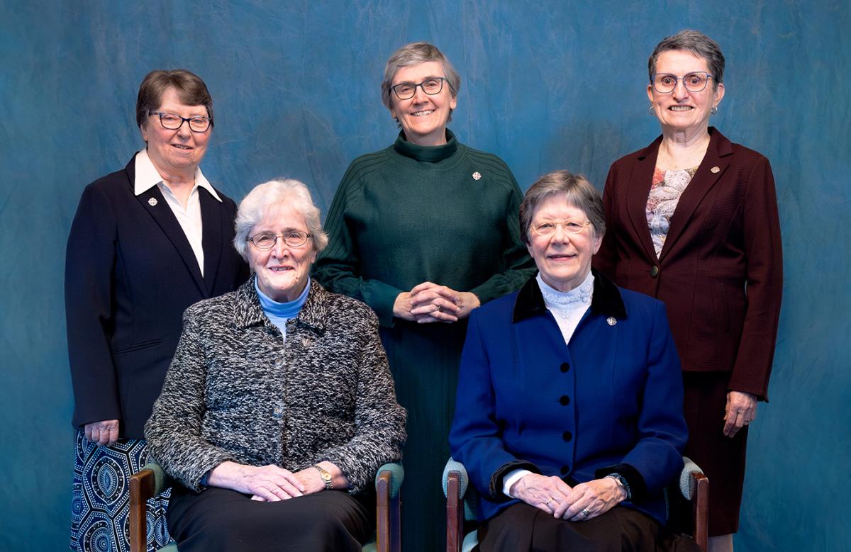 Group of five women in front of blue background.